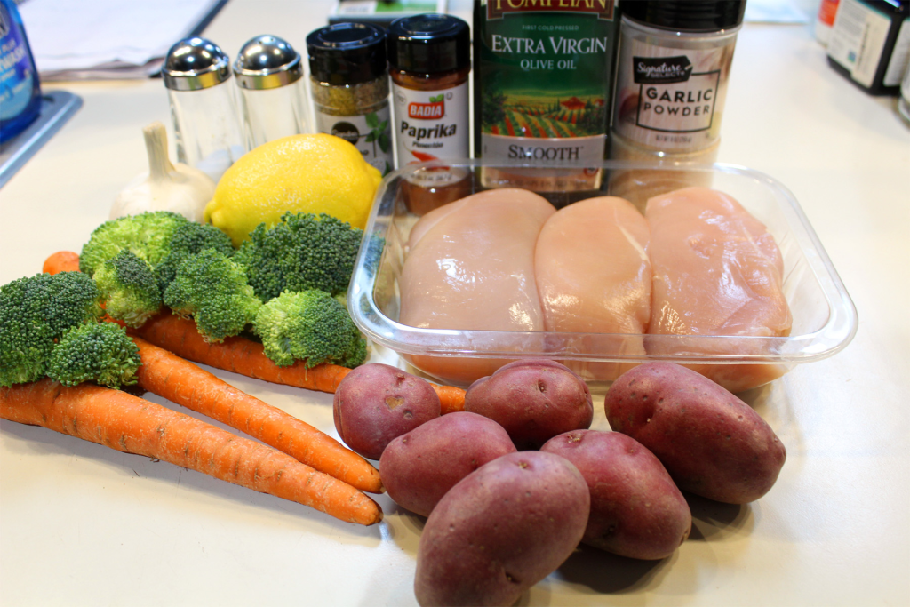 The raw ingredients to make lemon garlic chicken and roasted vegetables on a counter