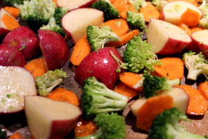 Close up of seasoned potatoes, broccoli, and carrots on a pan before being roasted