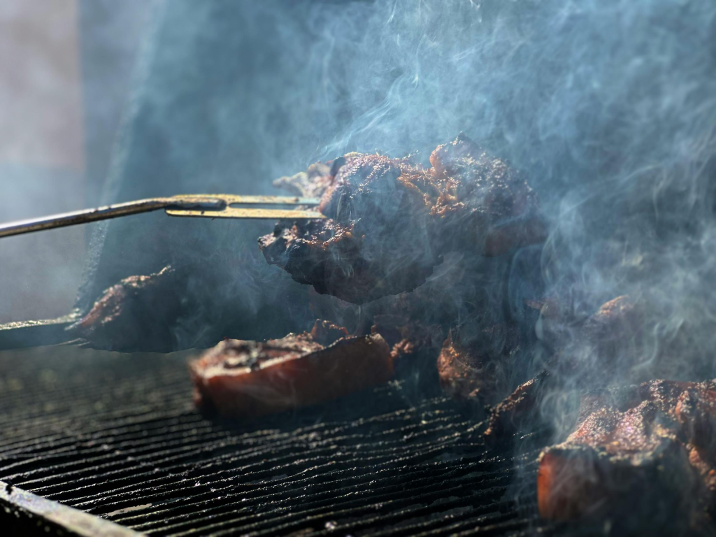 Close-up of meat sizzling on a smoky barbecue grill outdoors.