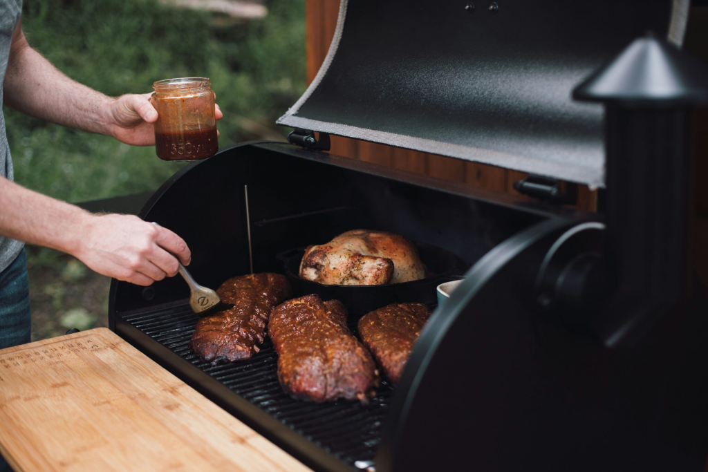 Person basting meat on a pellet grill outdoors.