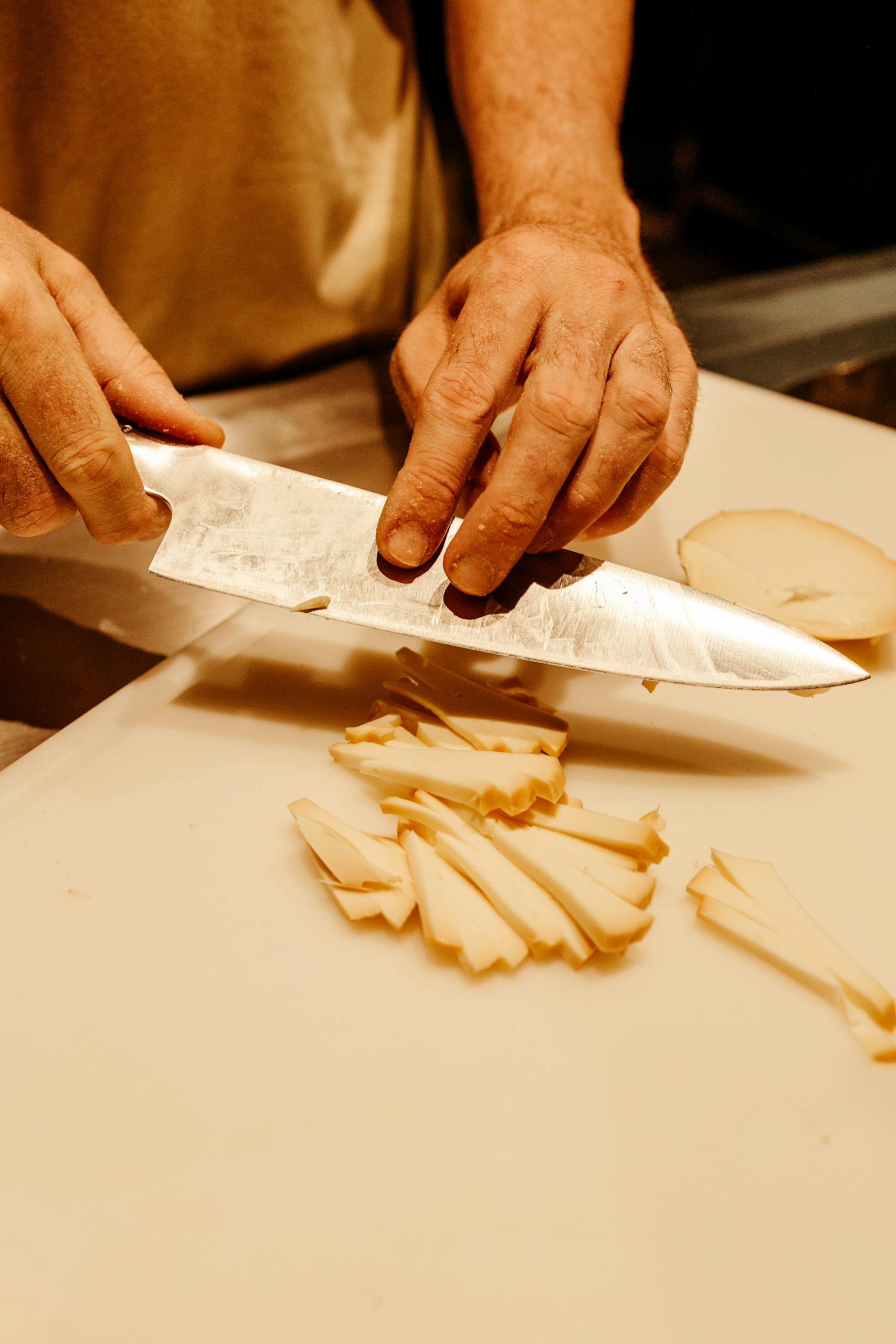 A chef skillfully slices potatoes with a sharp knife on a chopping board.