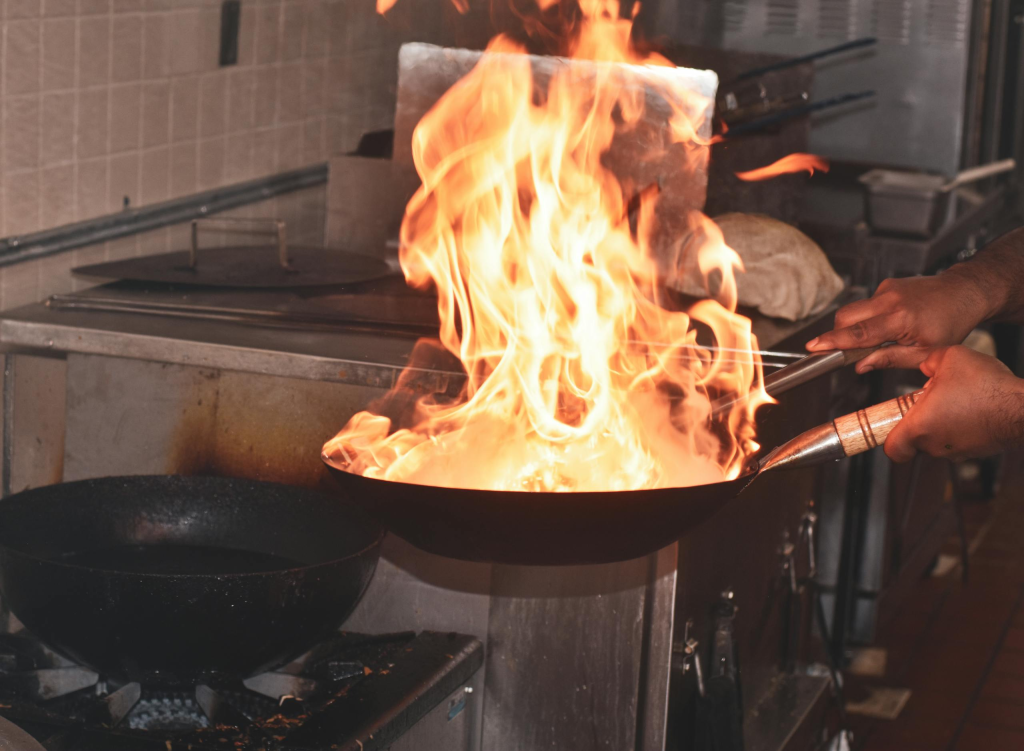 Chef expertly handles flaming pan in a bustling kitchen setting.