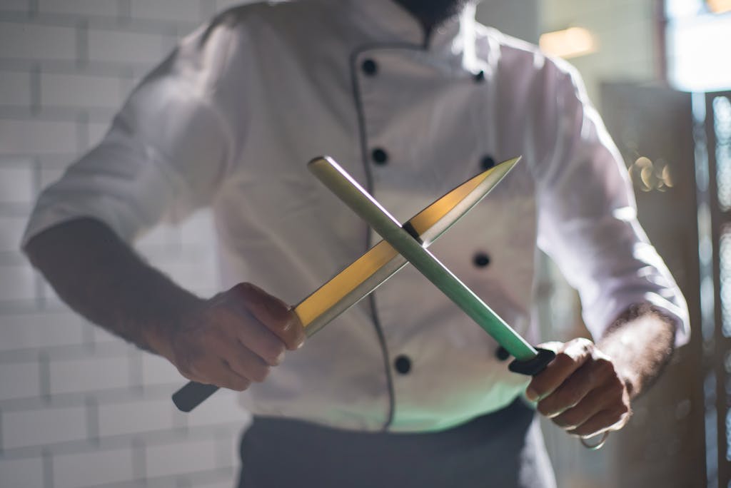 Close-up of a chef sharpening knives with a honing rod.