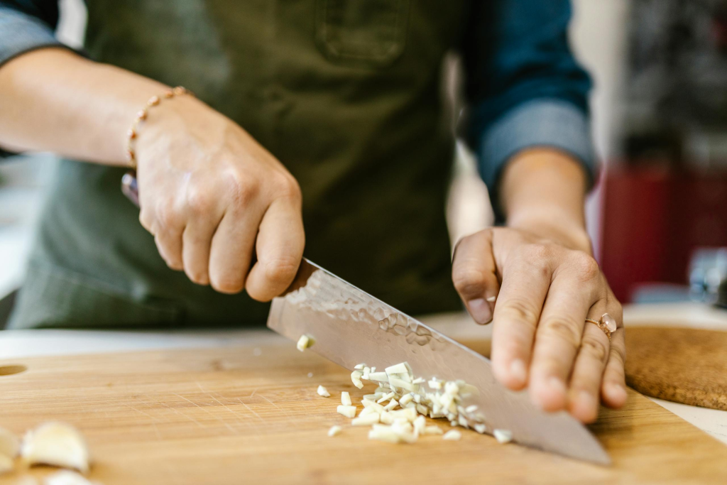 Close-up of a woman finely chopping garlic and properly handling a chefs knife using the pinch grip.