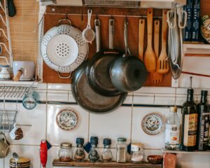 Collection of pans and culinary utensils near shelves with condiment bottles over gas stove at home
