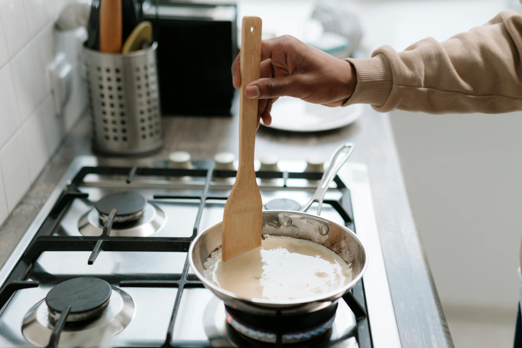 Person stirring a pan sauce on a gas stove, using a wooden spatula.