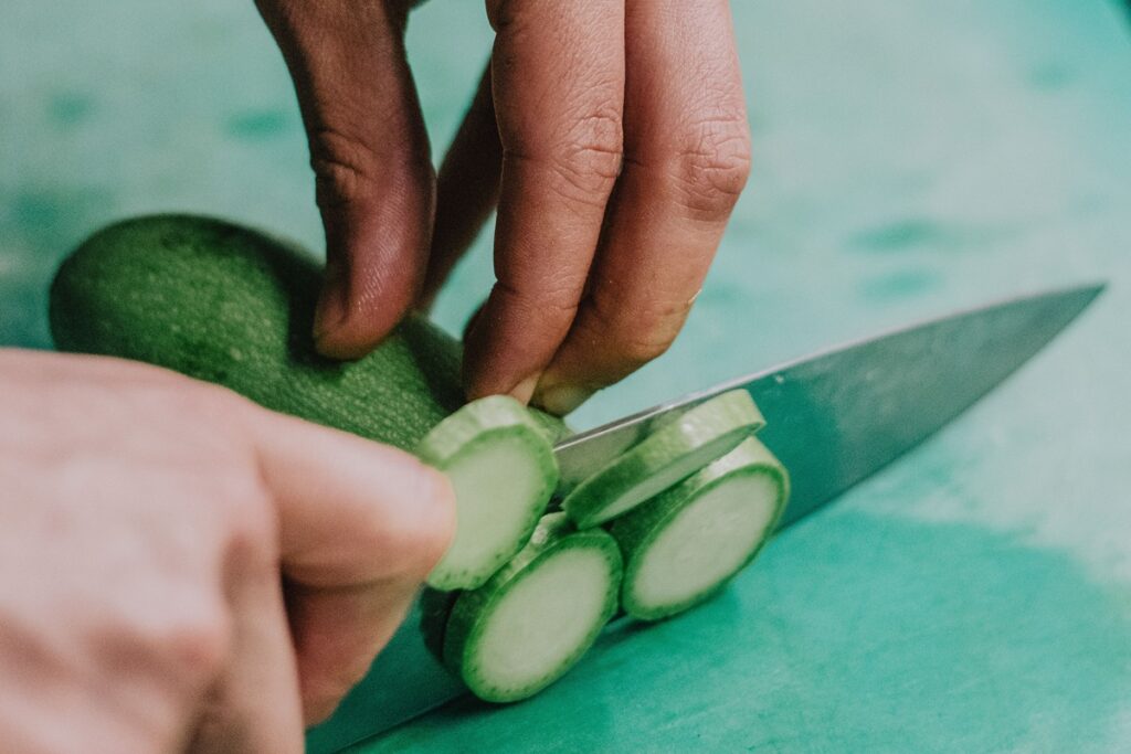 Person cutting a cucumber with a chef's knife and using their other hand as a guide hand.