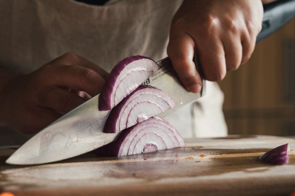 Man cutting an onion. He is holding the chef's knife with the pinch grip.
