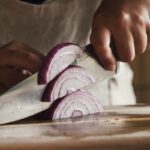 Man cutting an onion. He is holding the chef's knife with the pinch grip.