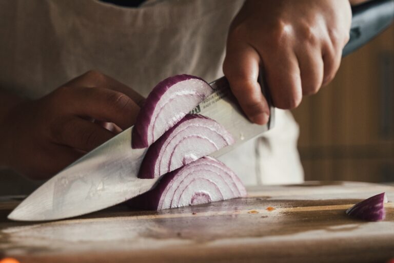 Man cutting an onion. He is holding the chef's knife with the pinch grip.