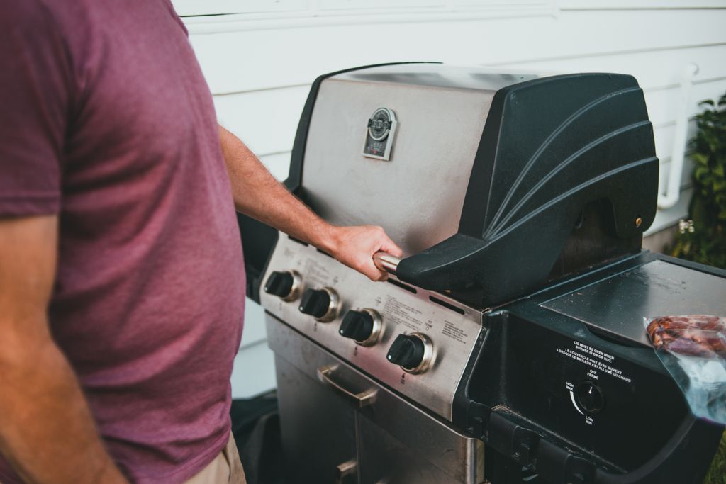 Adult man using a gas grill for two zone cooking.