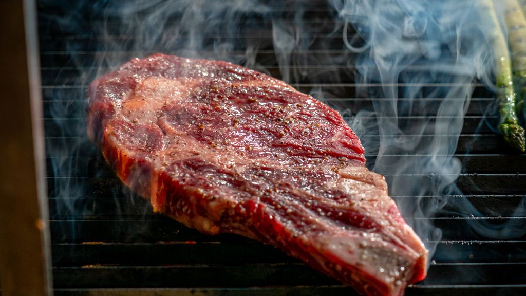 Close-up of a juicy steak sizzling on the grill with visible smoke, being seared.